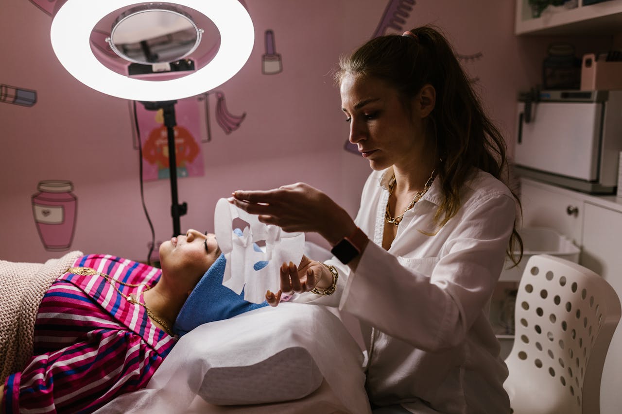 Aesthetician applying a sheet mask to a woman at a beauty salon for a rejuvenating facial treatment.
